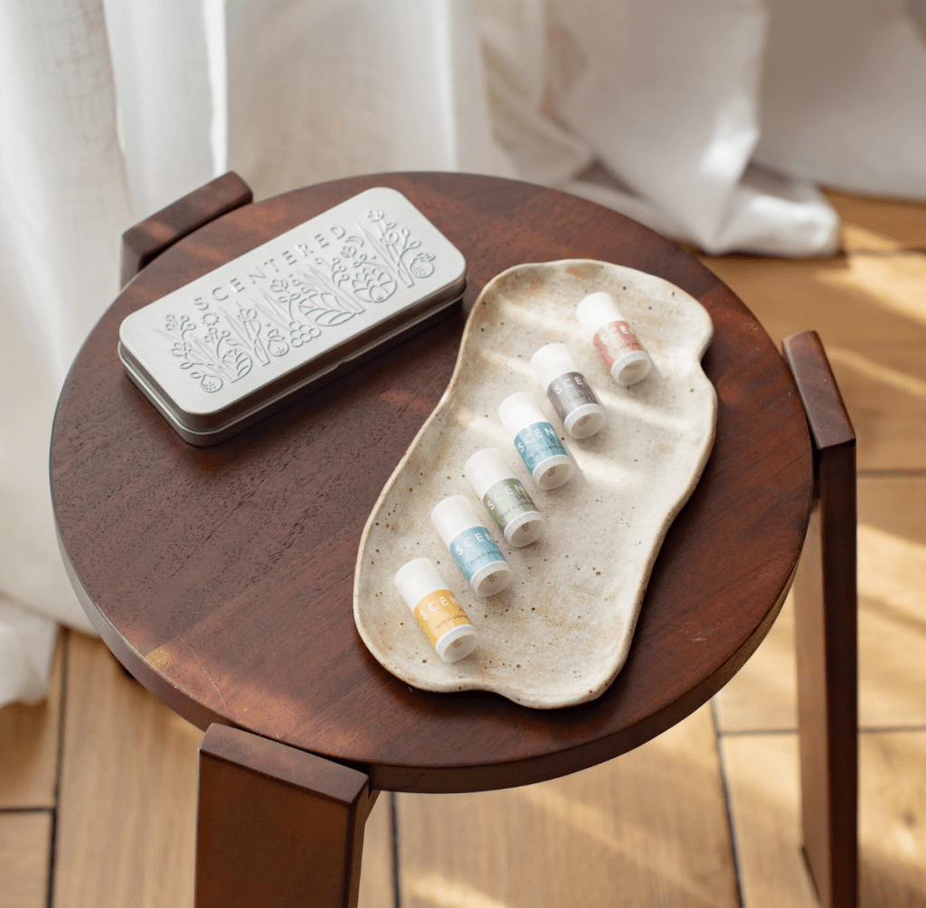 A neatly arranged Scentered Aromatherapy Balm Discovery tin and six mini balms in various colors, displayed on a textured tray, all resting on a wooden table.