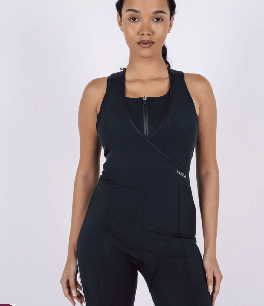 A model wearing the LUCA Road All-In-One bib shorts for women, showcasing a sleek design with a fitted top and supportive straps, presented against a neutral background.