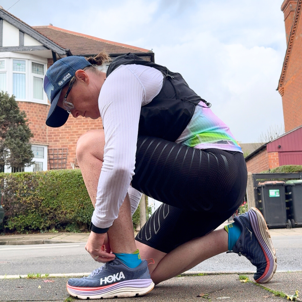 Photo of a woman adjusting her running shorts while holding a pair of trekking poles, showcasing the back of the shorts and a colorful top against an outdoor backdrop.