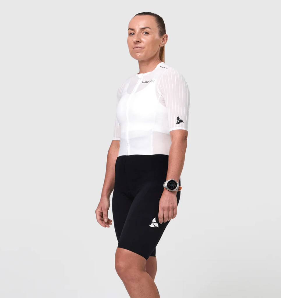 A triathlete wearing a white and black tri suit with short sleeves, standing confidently with a smartwatch on their wrist, against a plain background.