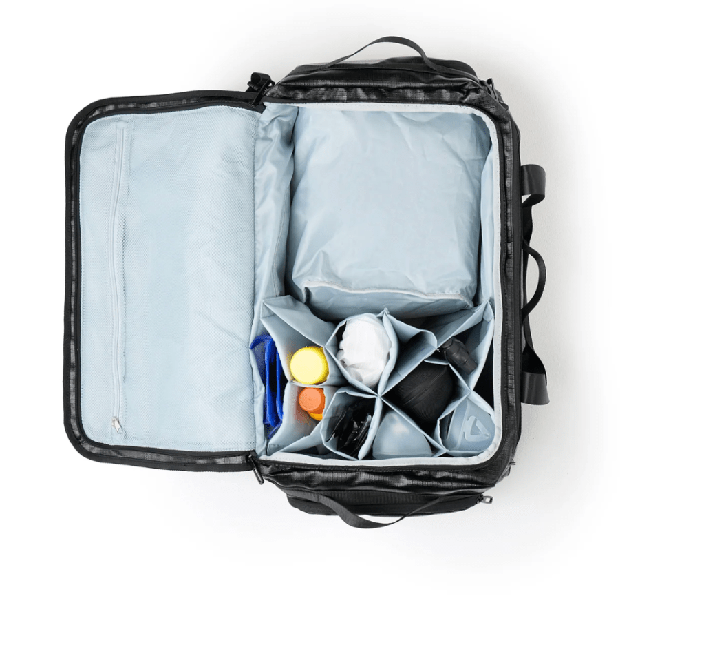 An open transition bag featuring multiple compartments for organizing triathlon gear, with items like water bottles and a pair of running shoes visible inside.