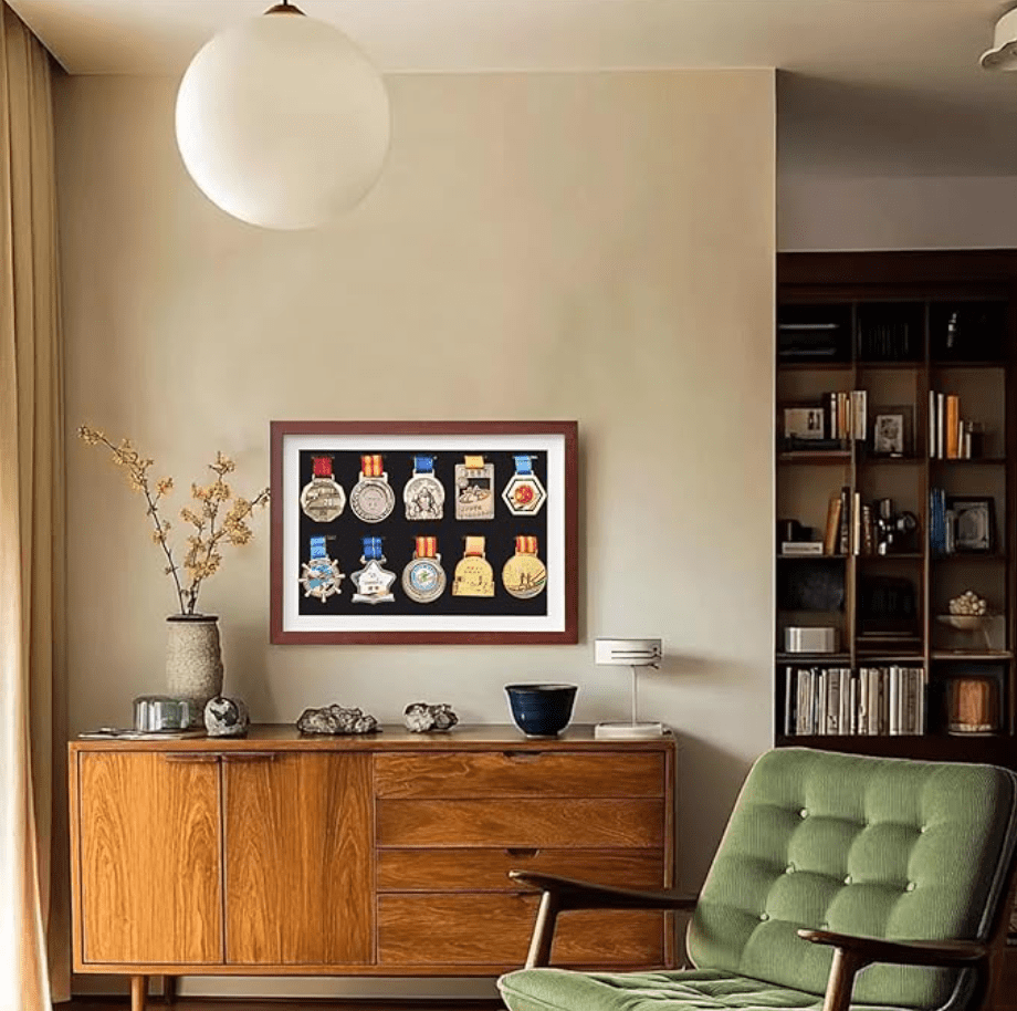 A framed collection of medals displayed on a wall, with a stylish wooden frame and decorative elements such as a vase and a small table. The background features a neutral-toned wall and modern furniture.